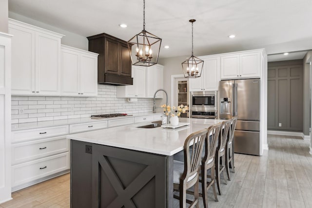 kitchen with tasteful backsplash, light countertops, appliances with stainless steel finishes, a kitchen island with sink, and a sink