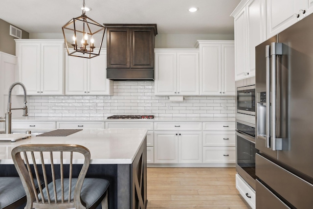 kitchen featuring stainless steel appliances, a breakfast bar, light countertops, tasteful backsplash, and decorative light fixtures