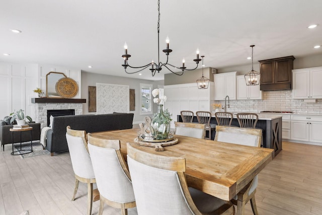 dining space featuring light wood-style floors, recessed lighting, a chandelier, and a stone fireplace