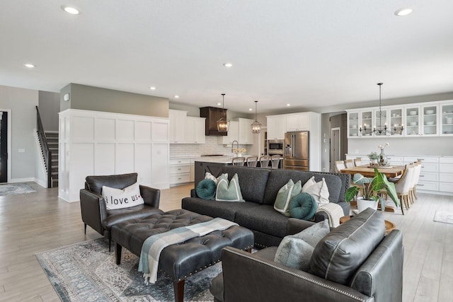 living area featuring stairs, light wood finished floors, recessed lighting, and a notable chandelier