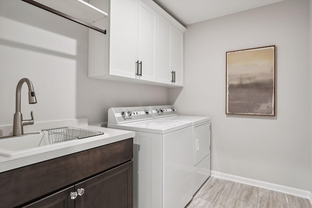 clothes washing area with baseboards, a sink, cabinet space, and washer and dryer