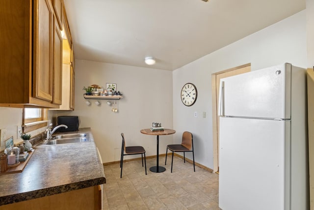 kitchen with baseboards, dark countertops, brown cabinets, freestanding refrigerator, and a sink