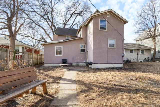 rear view of property featuring central air condition unit, fence, and stucco siding