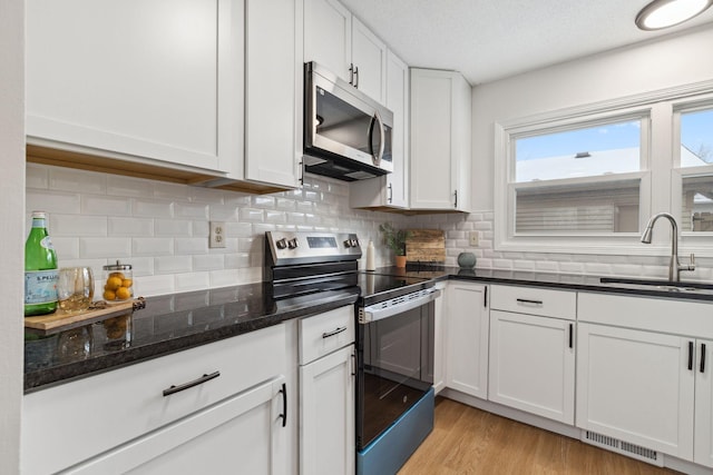 kitchen with appliances with stainless steel finishes, tasteful backsplash, white cabinets, light wood-type flooring, and sink