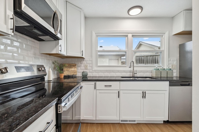 kitchen featuring sink, white cabinetry, dark stone counters, a textured ceiling, and stainless steel appliances