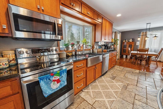 kitchen featuring stainless steel appliances, brown cabinets, a sink, and stone tile floors