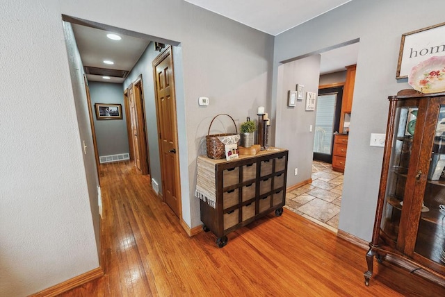 hall with baseboards, visible vents, and light wood-style floors