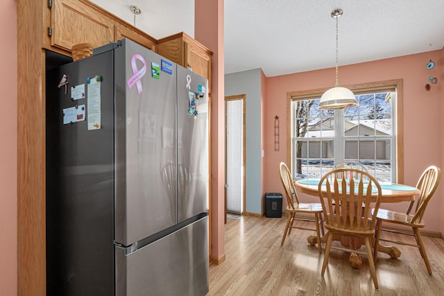 kitchen with a textured ceiling, light hardwood / wood-style flooring, stainless steel refrigerator, light brown cabinetry, and hanging light fixtures