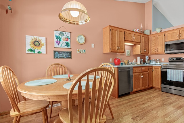 kitchen featuring decorative light fixtures, high vaulted ceiling, light wood-type flooring, and appliances with stainless steel finishes