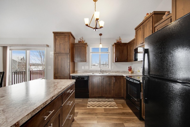 kitchen with black appliances, a notable chandelier, wood-type flooring, pendant lighting, and sink