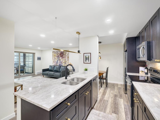 kitchen featuring light stone countertops, pendant lighting, appliances with stainless steel finishes, sink, and light wood-type flooring