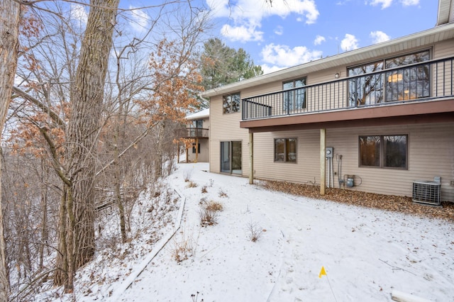 snow covered house featuring a balcony and central AC unit