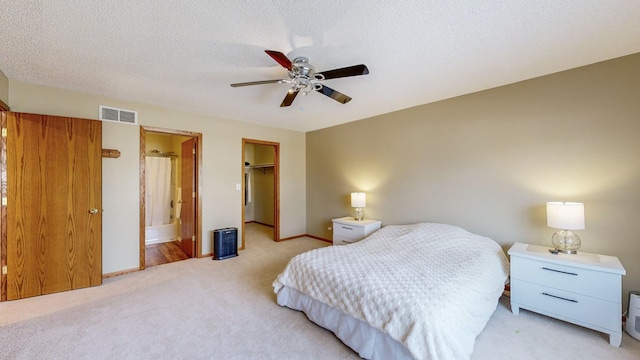 carpeted bedroom featuring a textured ceiling, a walk in closet, a closet, ceiling fan, and ensuite bathroom