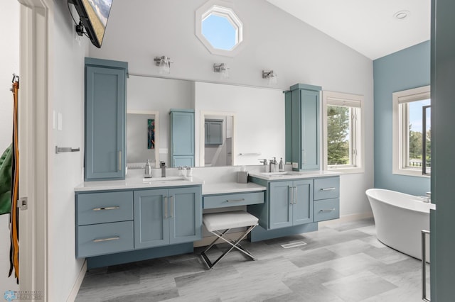 bathroom featuring lofted ceiling, a tub to relax in, and vanity