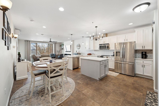 kitchen featuring white cabinets, ceiling fan with notable chandelier, hanging light fixtures, appliances with stainless steel finishes, and a kitchen island