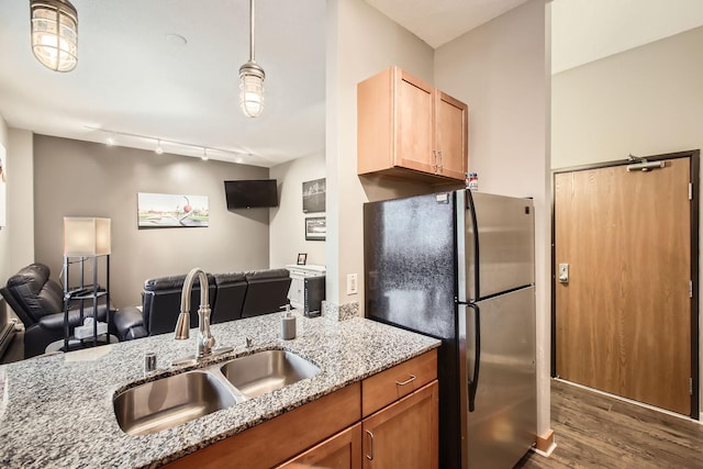 kitchen featuring pendant lighting, track lighting, sink, stainless steel fridge, and light stone countertops