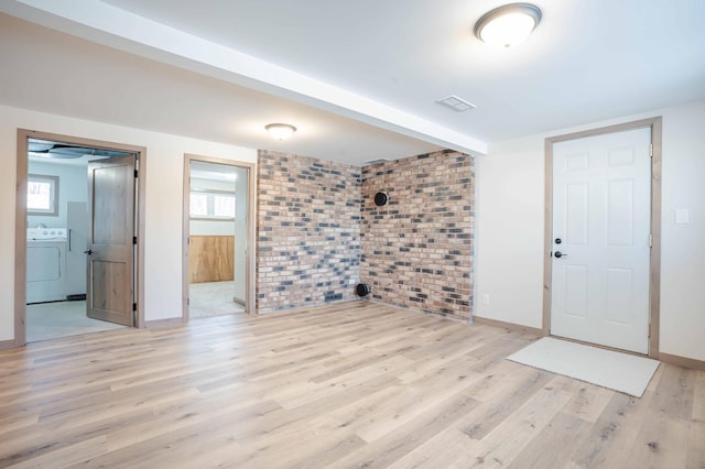 interior space with brick wall, washer / clothes dryer, and light hardwood / wood-style floors