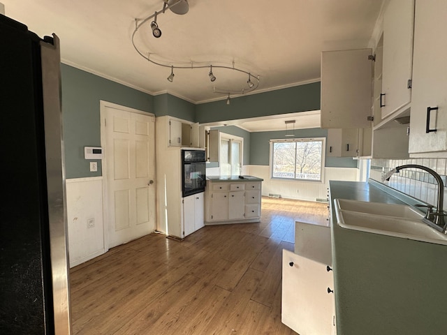 kitchen featuring crown molding, sink, white cabinets, light hardwood / wood-style floors, and oven