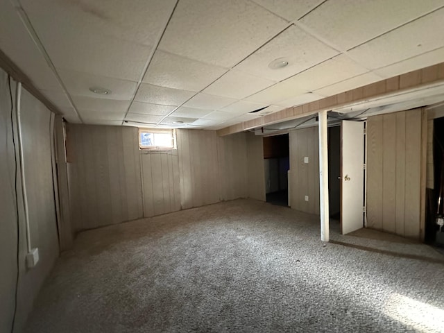 basement with carpet flooring, a drop ceiling, and wooden walls