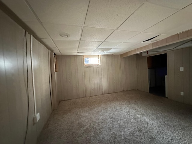 basement featuring a paneled ceiling, carpet floors, and wood walls