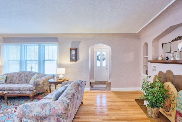 living room with built in shelves, a textured ceiling, and light hardwood / wood-style flooring