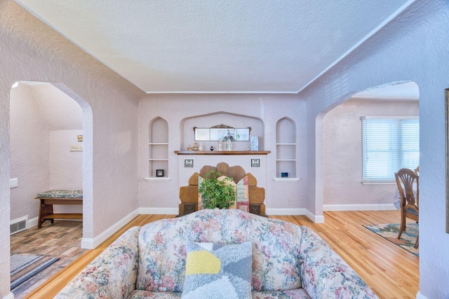 living room with a textured ceiling, built in features, and wood-type flooring