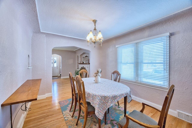 dining space with a textured ceiling, a healthy amount of sunlight, a notable chandelier, and light hardwood / wood-style flooring