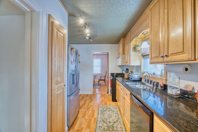 kitchen with sink, stainless steel appliances, light hardwood / wood-style floors, and dark stone counters