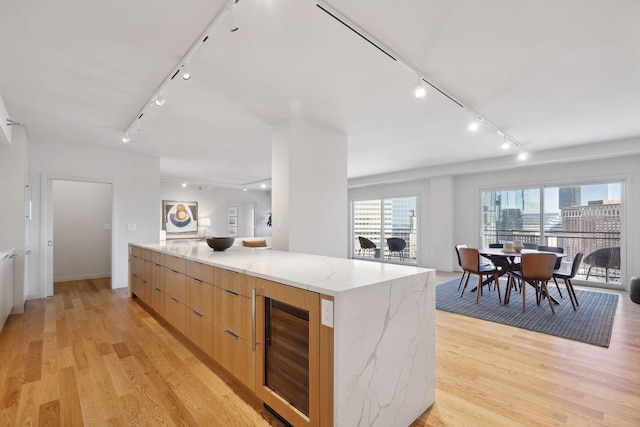 kitchen featuring light stone counters, light hardwood / wood-style floors, beverage cooler, and a spacious island