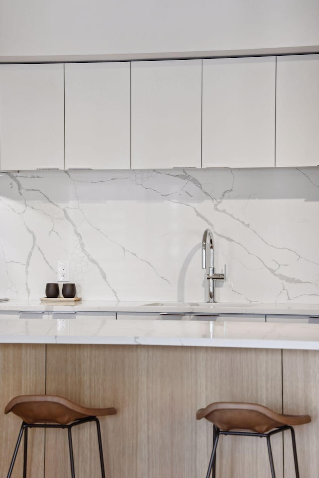 kitchen with light stone counters, a kitchen bar, and white cabinets