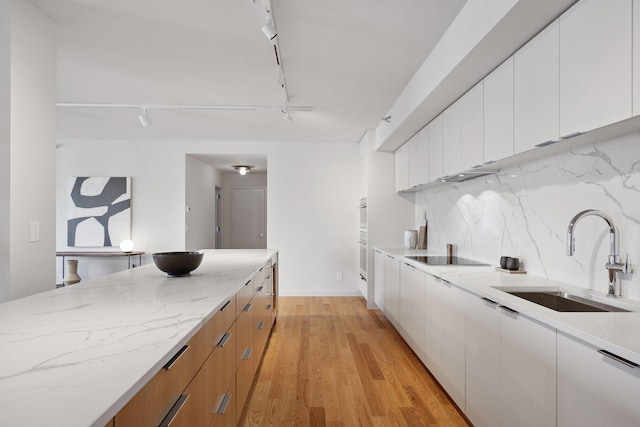 kitchen featuring rail lighting, sink, white cabinets, light stone countertops, and backsplash