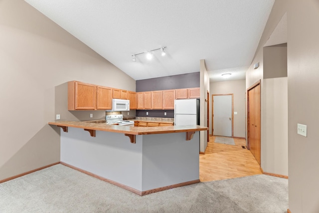 kitchen with white appliances, kitchen peninsula, a breakfast bar, rail lighting, and light carpet