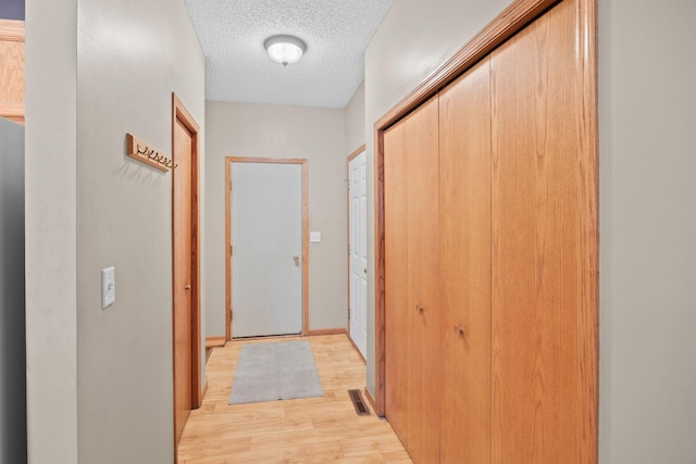 hall with a textured ceiling and light hardwood / wood-style flooring