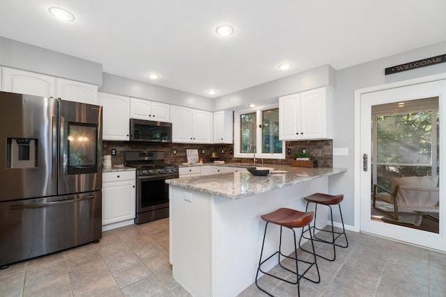 kitchen with white cabinets, appliances with stainless steel finishes, kitchen peninsula, and light stone countertops