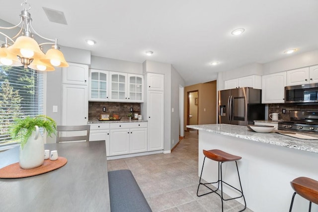 kitchen with backsplash, white cabinets, decorative light fixtures, and appliances with stainless steel finishes