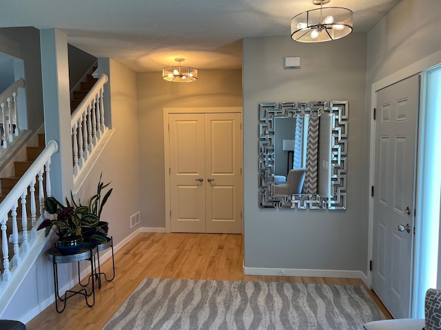 entrance foyer with a notable chandelier, light wood finished floors, visible vents, stairway, and baseboards