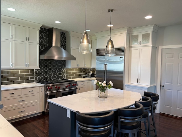 kitchen with premium appliances, light stone counters, hanging light fixtures, wall chimney range hood, and glass insert cabinets