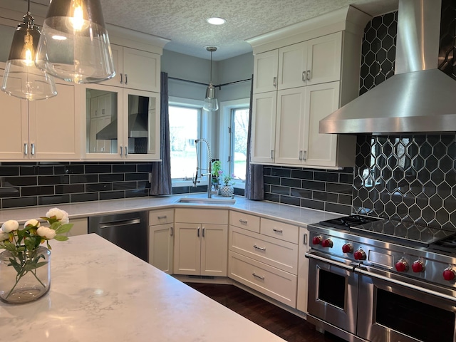 kitchen featuring wall chimney exhaust hood, glass insert cabinets, appliances with stainless steel finishes, decorative light fixtures, and white cabinetry