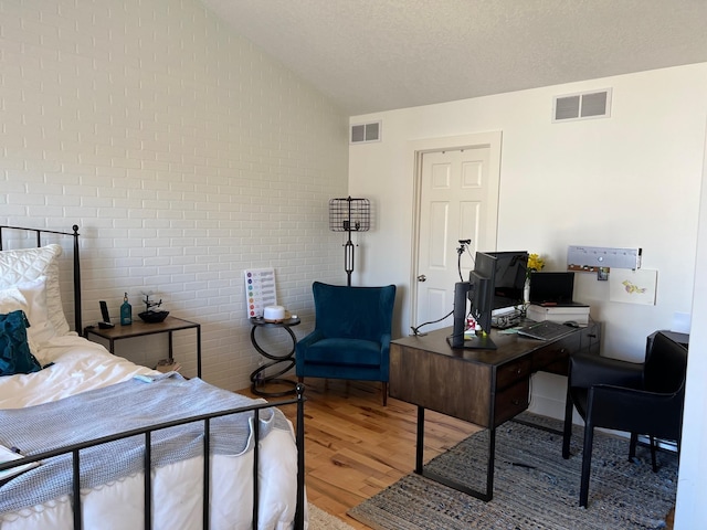 bedroom featuring lofted ceiling, a textured ceiling, wood finished floors, and visible vents