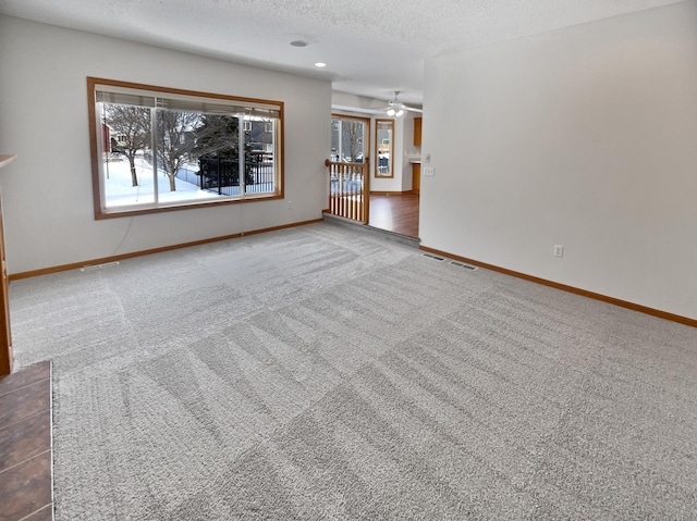 unfurnished living room featuring ceiling fan, a textured ceiling, and dark colored carpet