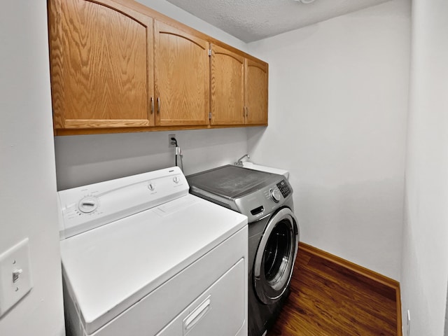 laundry room with washing machine and dryer, dark wood-type flooring, cabinets, and a textured ceiling