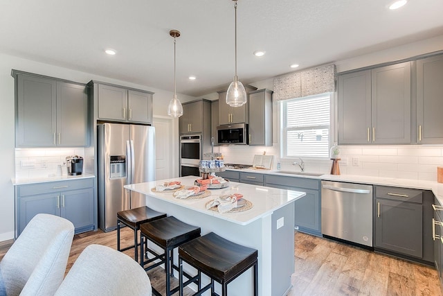 kitchen featuring sink, light wood-type flooring, decorative light fixtures, a kitchen island, and stainless steel appliances