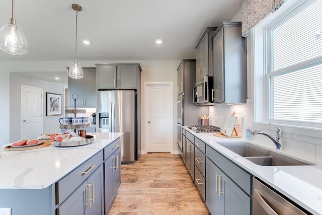 kitchen with appliances with stainless steel finishes, light wood-type flooring, tasteful backsplash, sink, and decorative light fixtures