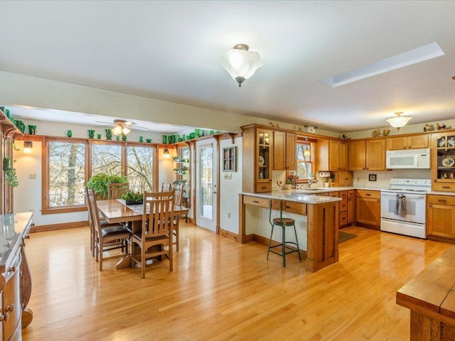 kitchen with sink, a kitchen bar, ceiling fan, white appliances, and light hardwood / wood-style flooring