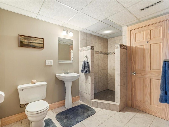 bathroom with tile patterned flooring, tiled shower, a paneled ceiling, and toilet