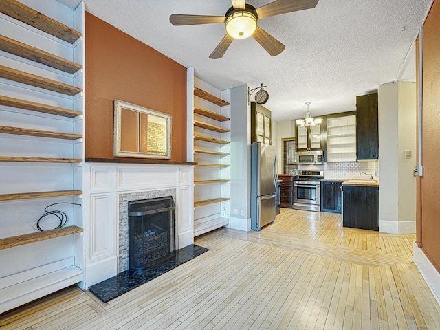 unfurnished living room with sink, a textured ceiling, a fireplace, light hardwood / wood-style floors, and ceiling fan with notable chandelier