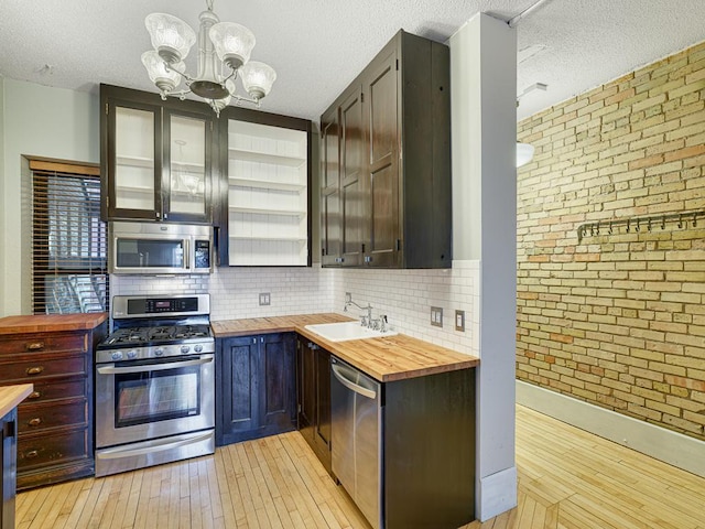 kitchen featuring pendant lighting, brick wall, wooden counters, appliances with stainless steel finishes, and sink