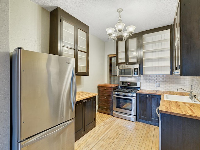 kitchen featuring sink, a textured ceiling, butcher block countertops, hanging light fixtures, and appliances with stainless steel finishes