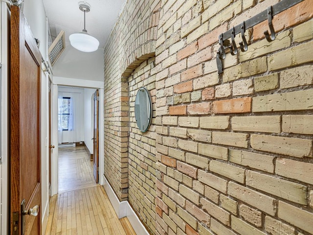 corridor with light wood-type flooring and brick wall