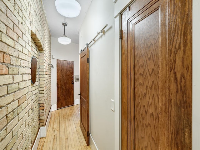 hallway featuring brick wall, light wood-type flooring, and a barn door